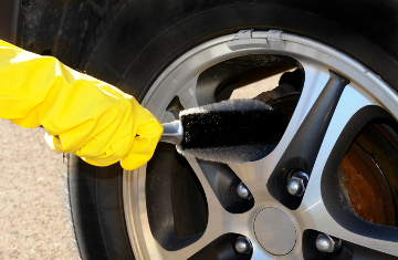 Woman’s hand with a rim brush cleaning a wheel of an SUV car